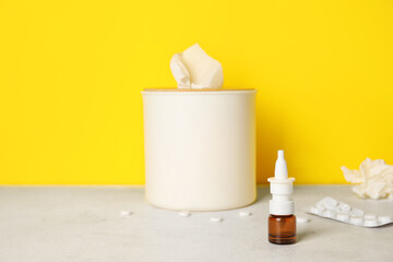 Fototapeta na wymiar Nasal drops with pills and tissue box on table near yellow wall. Allergy concept
