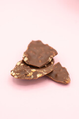 broken bar of milk chocolate with flakes on pastel pink background