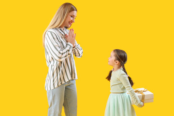 Cute little girl surprising her mother with gift on yellow background
