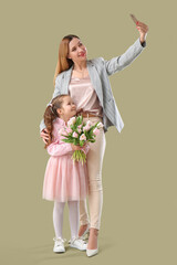 Cute little girl with tulips and her mother taking selfie on green background