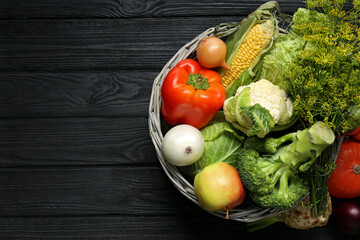 Different fresh vegetables in wicker basket on black wooden table, top view with space for text. Farmer harvesting