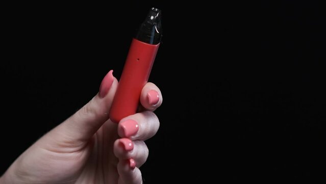Red color vape pod system with replaceable cartridges in female hands isolated on black background. The concept of modern smoking, vaping and nicotine
