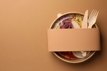 Tasty food in container with wooden fork and knife on beige background, top view. Space for text