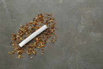 Hand rolled cigarette and tobacco on dark grey table, top view. Space for text