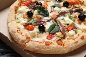 Tasty pizza with anchovies, basil and olives in cardboard box, closeup