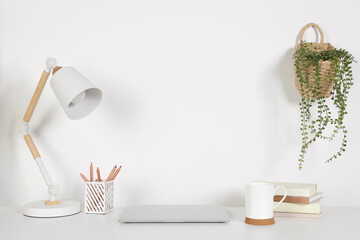 Cozy workspace with laptop, lamp and stationery on white desk at home