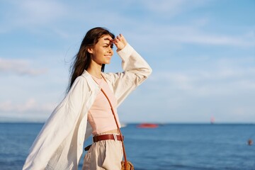 A girl with her eyes closed in the sun against an ocean backdrop smiling with teeth, flying hair,...