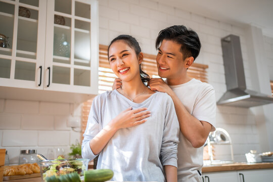 Asian romantic man making surprise girlfriend with necklace in kitchen. 