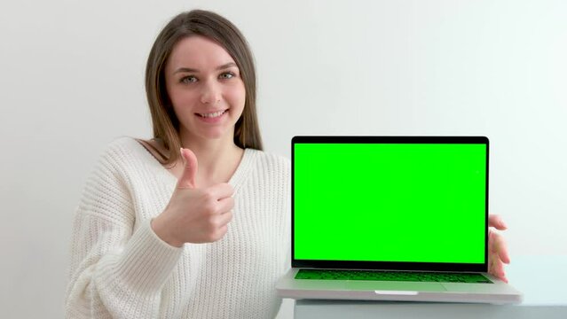 Over the shoulder shot of business woman working in office interior on pc on desk, looking at green screen. Office person using laptop computer with laptop green screen sitting at wooden table