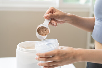 Diet meal replacement for weight loss, asian young woman in sportswear, hand in holding scoop making protein into bottle to shake, drink supplement for muscle after workout at home. Healthy body care.
