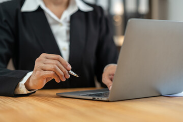 Confident businesswoman, financial advisor sitting typing report and point to income data Company earnings from information documents piled up on the desk on laptop computer screen in office.