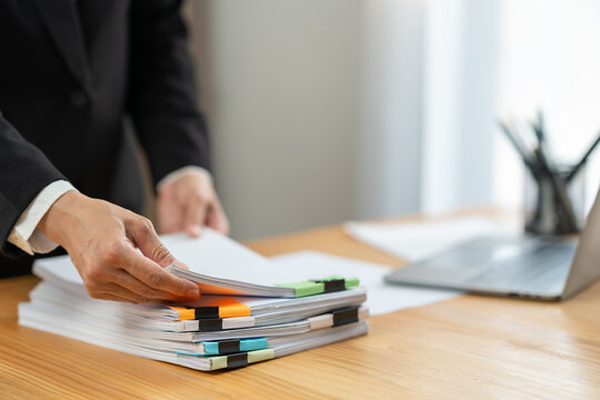 Businesswoman in black suit working at desk with documents preparation, searching, sifting through information related to financial, earnings, taxes of company to prepare for meeting in office.