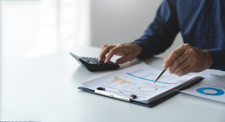 Investing young businessman accountant using calculator for income-expense calculation and planning pointing to database showing graph chart real estate business income finance and tax system concept