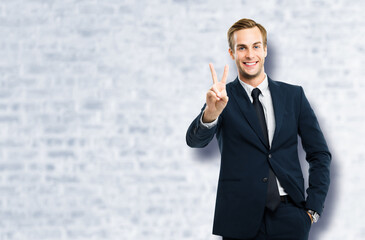 Excited businessman in black confident suit showing two fingers or victory sign gesture, white...