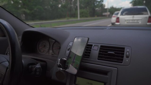 View from inside car on dashboard with smartphone. Mobile phone with gps navigation fixed in mounting. App map for travel. CMan use GPS navigation in phone with online map on screen while driving car.