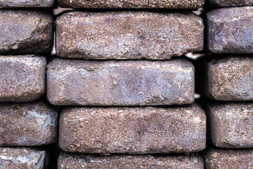 Close up macro photograph of a pile of recycled red or brown weathered concrete masonry pavers with rounded corners and chipped edges sitting in vertical stacks.