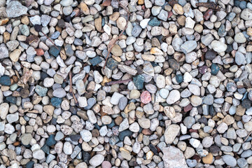 Close up background photograph of dry pea gravel stone or rock garden with rounded edges and muted white, blue, pink, brown and yellow colors.