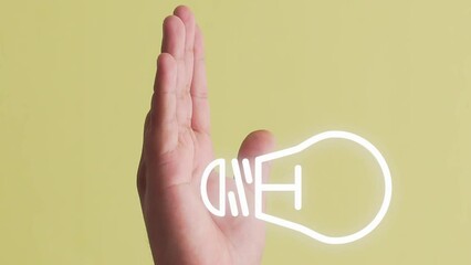Light bulb symbol or idea animation appearing on a hand. Yellow background. Vertical shot.