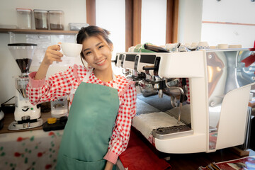 Beautiful asian coffee girl wearing apron  standing and holding a cup with smile in coffee shop.