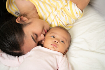 Loving Asian Mom carying of her newborn baby at home in the bedroom. happy family. mother playing with her baby in the bedroom. Mother hugging her little 2 months old Girl.