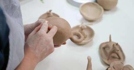 woman forming clay cup shape by hands, closeup in artistic studio