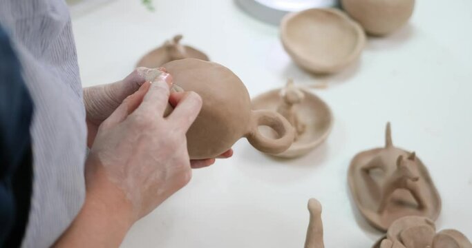 woman forming clay cup shape by hands, closeup in artistic studio