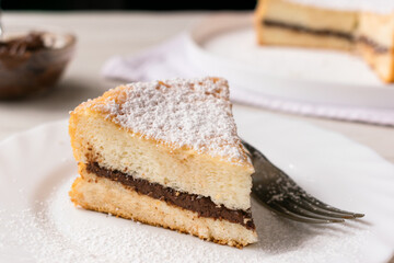A slice of Angel Cake filled with hazelnut spread and garnished with powdered sugar, on a white plate and white background