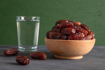 Glass of water with a bowl of date fruit on green background 