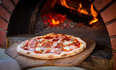 Selbstklebende Fototapeten Chef placing pizza in brick oven © InversedSlayer
