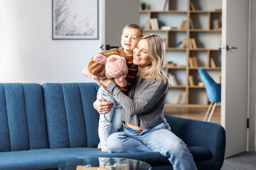 Young pregnant woman and her son sit on sofa at home, little boy spend time together, enjoy...