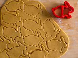 Close-up kneaded ginger dough and carved figurines from it. The shapes of rabbit. Cutting sugar cookie dough with Easter shaped cookie cutters. Preparation for Easter. Holidays baking.