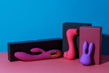 Different dildo vibrators and vacuum clitor stimulators with gift boxes on colored background