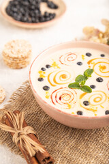 Yoghurt with bilberry and caramel in ceramic bowl on gray concrete, side view, selective focus.