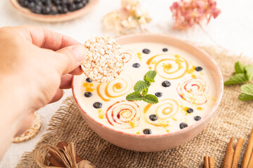 Yoghurt with bilberry and caramel in ceramic bowl on gray concrete, hand dipping cookies in yogurt,...