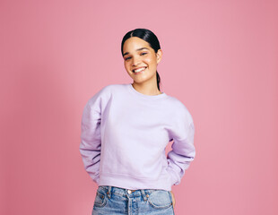 Female in her 20s looking at the camera in a studio, standing against a pink background