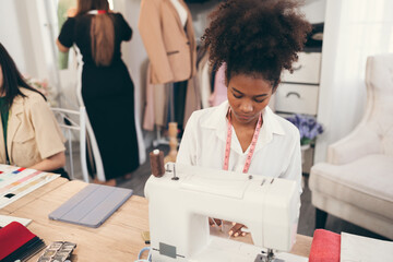 Happy beautiful African American woman fashion designer clothes working with sewing in own dressmaking studio or boutique	
