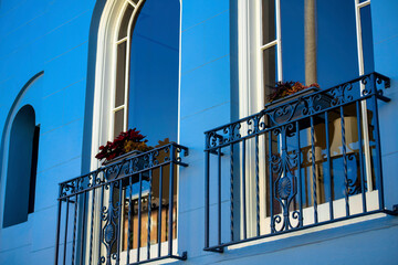 Small decorative balconies with twisted metal frames and flower planters on railing with blue stucco facade and windows