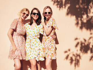 Fototapeta na wymiar Three young beautiful smiling hipster female in trendy summer dresses clothes. Sexy carefree women posing in the street. Positive models having fun, talking, chatting. Going crazy. In sunglasses