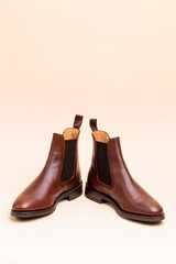 Closeup of Pair of Classic Leather Chealsea Boots As Still Life Concepts Placed On One Another Over Beige Background.