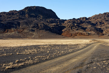 Fototapeta na wymiar piste de terre et de gravier avec un sol volcanique composé de sale noir au bout du monde suite à un voyage en Islande 