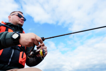 Fishing rod in the hands of a fisherman close-up. Summer fishing. Blue sky on the background. Selective focus on the hands