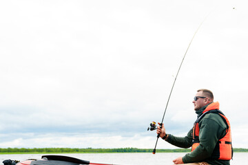 A fisherman throws a fishing rod into the water while sitting in an inflatable boat
