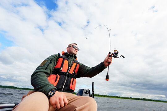 Porter of a fisherman sitting in a boat. A man with a spinning rod in his hands. Photo on a wide-angle lens