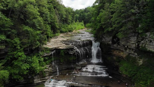 Cummins Falls aerial drone shot panning down with waterfalls, lush green forest and river rocks.