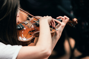 A musician playing the violin in a string section of a classical symphony orchestra rehearsal