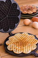 An antique waffle iron with a freshly baked waffle next to it are country eggs and a dish with freshly baked waffles