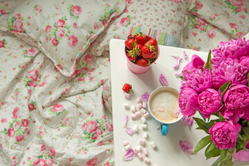 Sweet strawberries and coffee with milk among peony flowers by the bed in Provence style.
