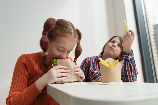 Couple Of Cute Elementary Age Kids Eating Fast Food For Lunch. Two Little Children From Ukraine Enjoying The Meal In A European Cafe