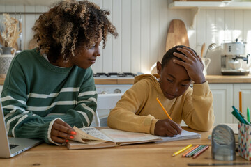 Young African American woman homeschool mom helping son with homework, mother and child studying at...