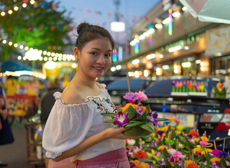 Portrait of Asian Thai woman with Loy Krathong in Thailand , floating on water in local street...